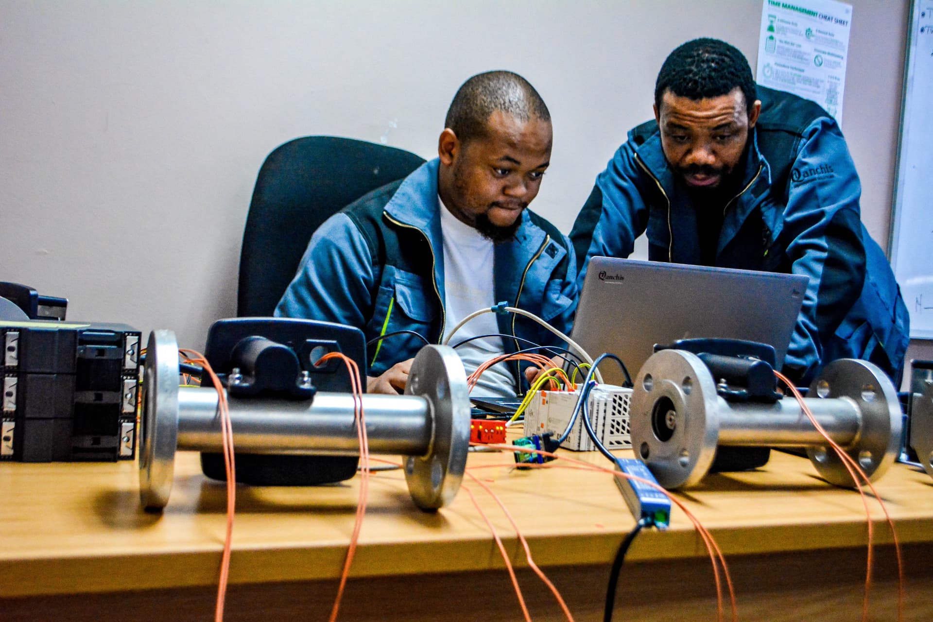 Two Qanchis engineers configuring a flow-meter test bench on a laptop